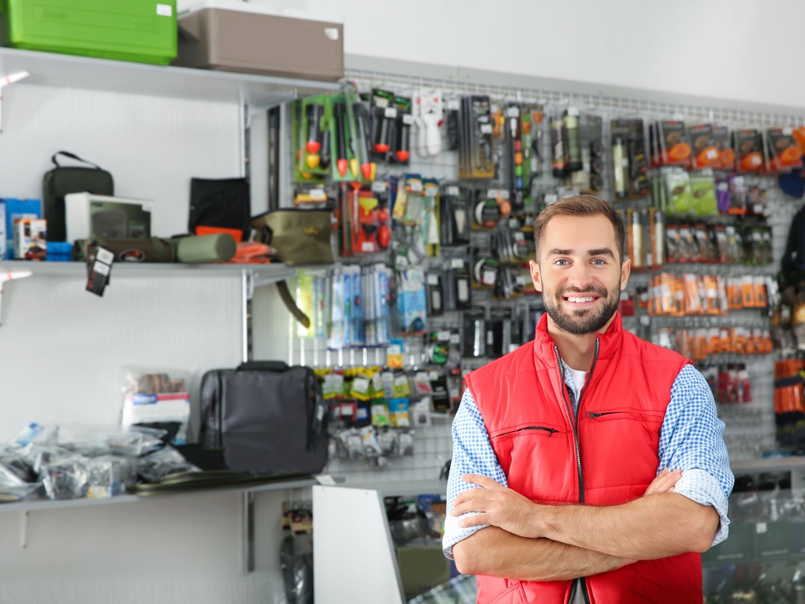 Hardware store owner in a red vest smiling in front of stocked shelves