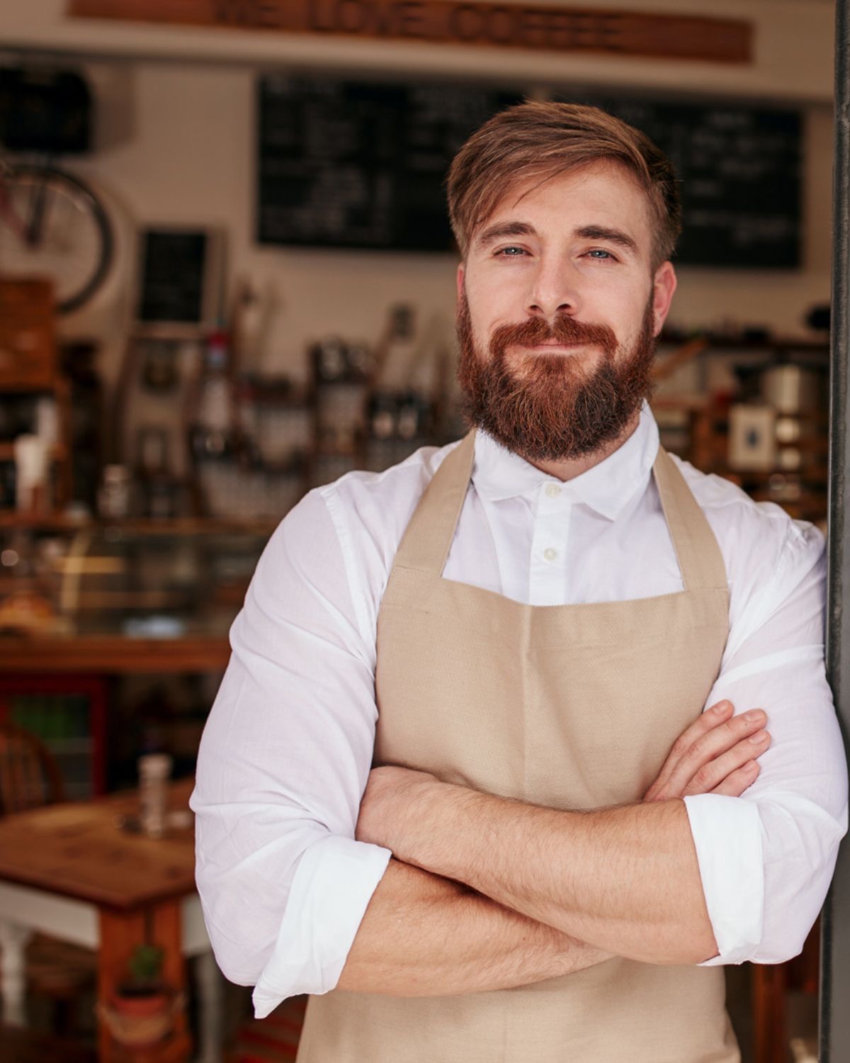 Smiling café owner in an apron, arms crossed, standing in his shop